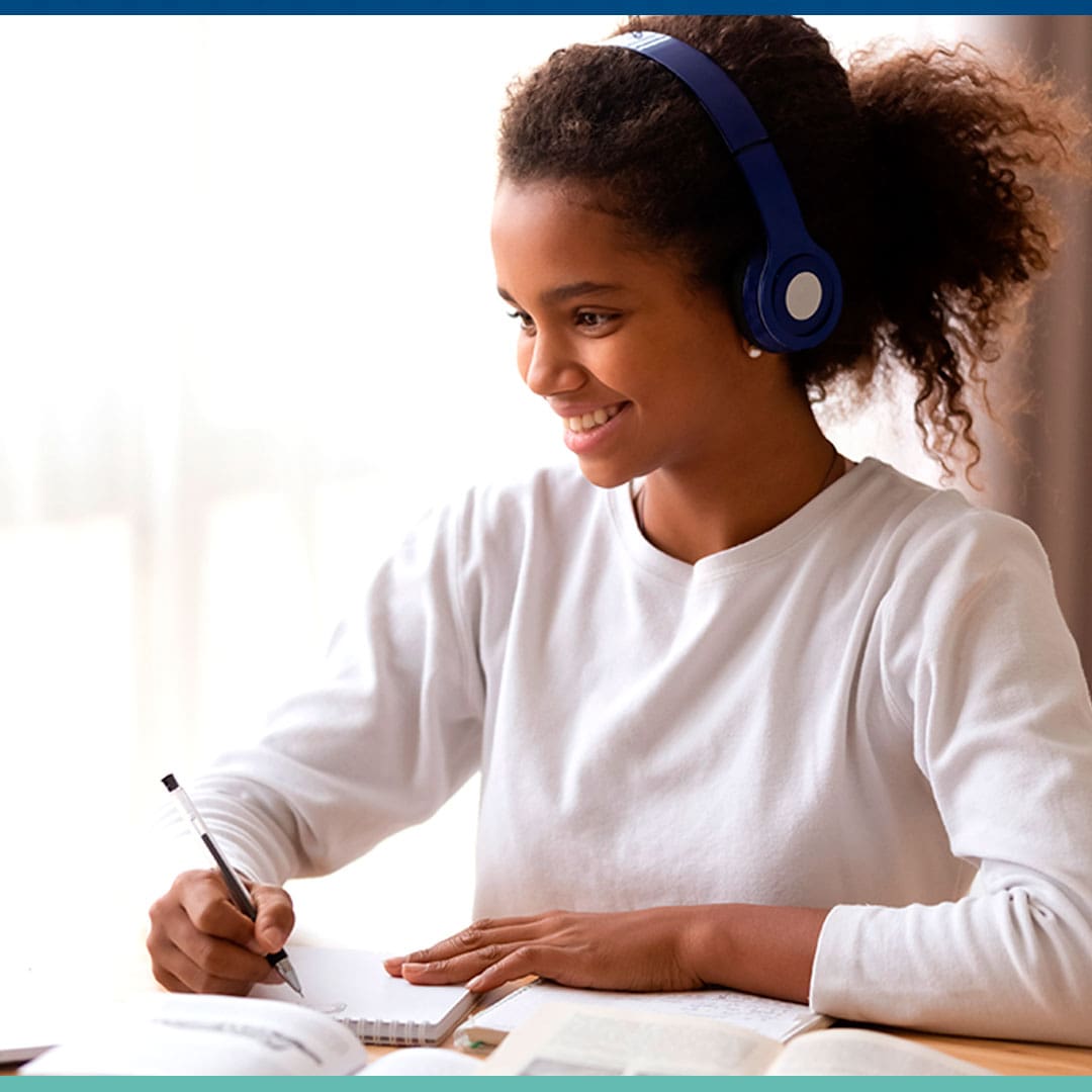 Garota assistindo aula online e fazendo anotações no caderno