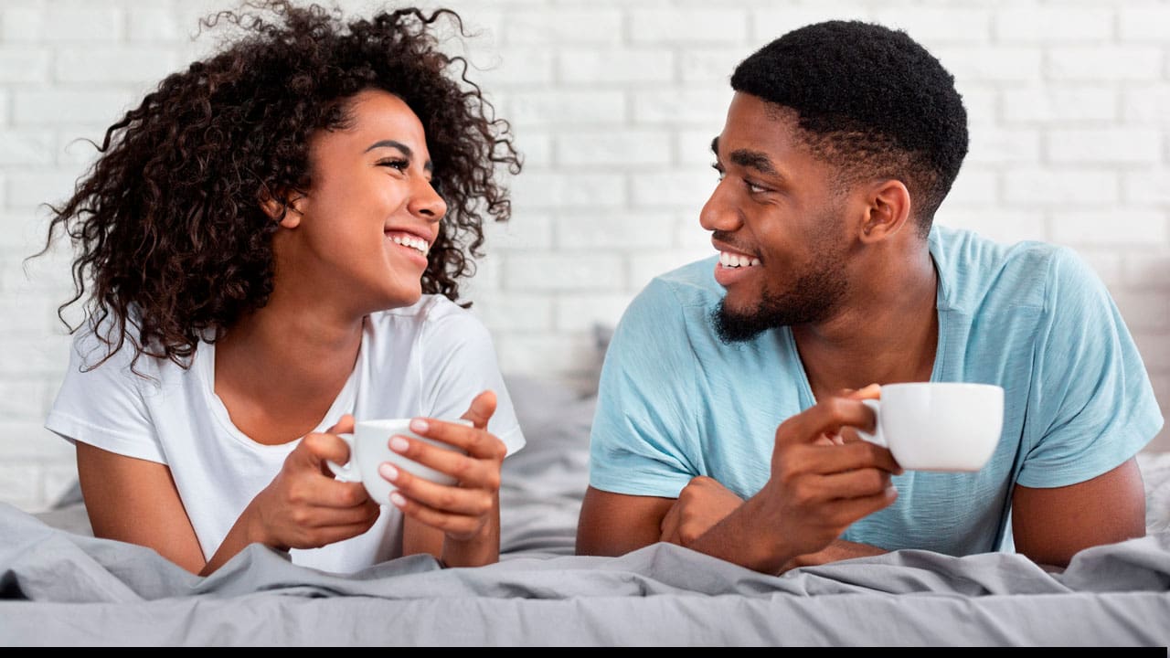 Casal na cama com xícaras de café nas mãos