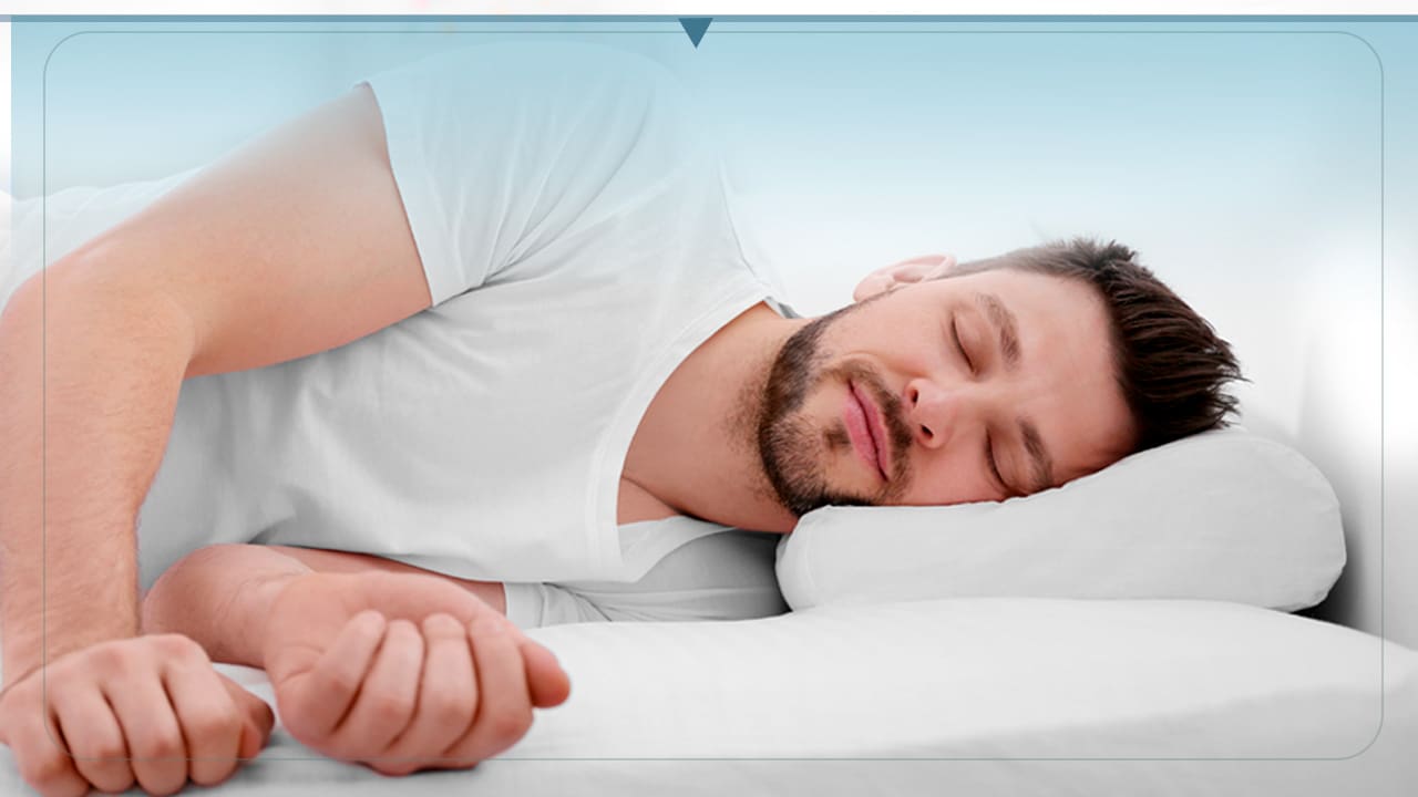 imagem mostra homem dormindo em uma cama confortável com lençóis e travesseiros brancos