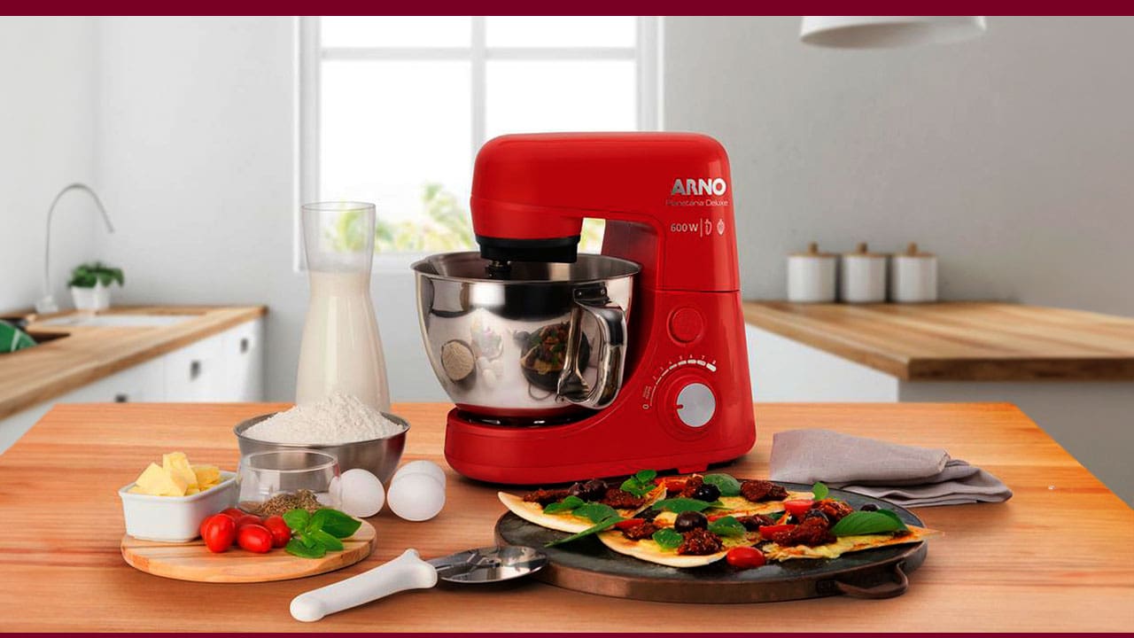 imagem frontal frente Batedeira Planetária Arno Nova Deluxe vermelha vermelho prata cinza brilho reflexo equipamento mesa bancada marrom madeira massas cortadas ingredientes queijo tempero ovos brancos pegador colher jarra leite guardanapo fundo janela potes brancos vaso planta verde parede branca