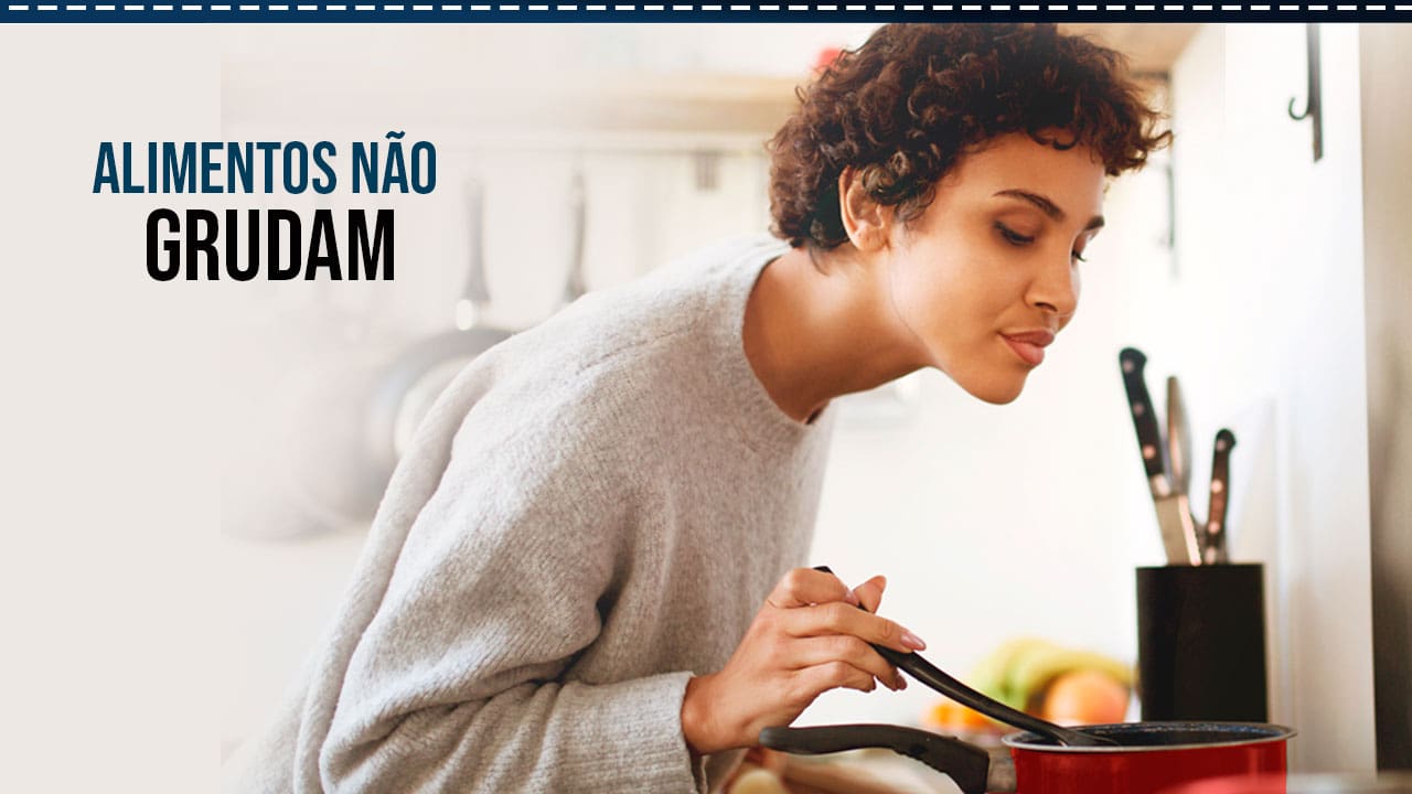 moça mulher jovem cabelo curto observando olhando panela preparo blusa cinza fundo facas frigideiras penduradas parede alimentos não grudam