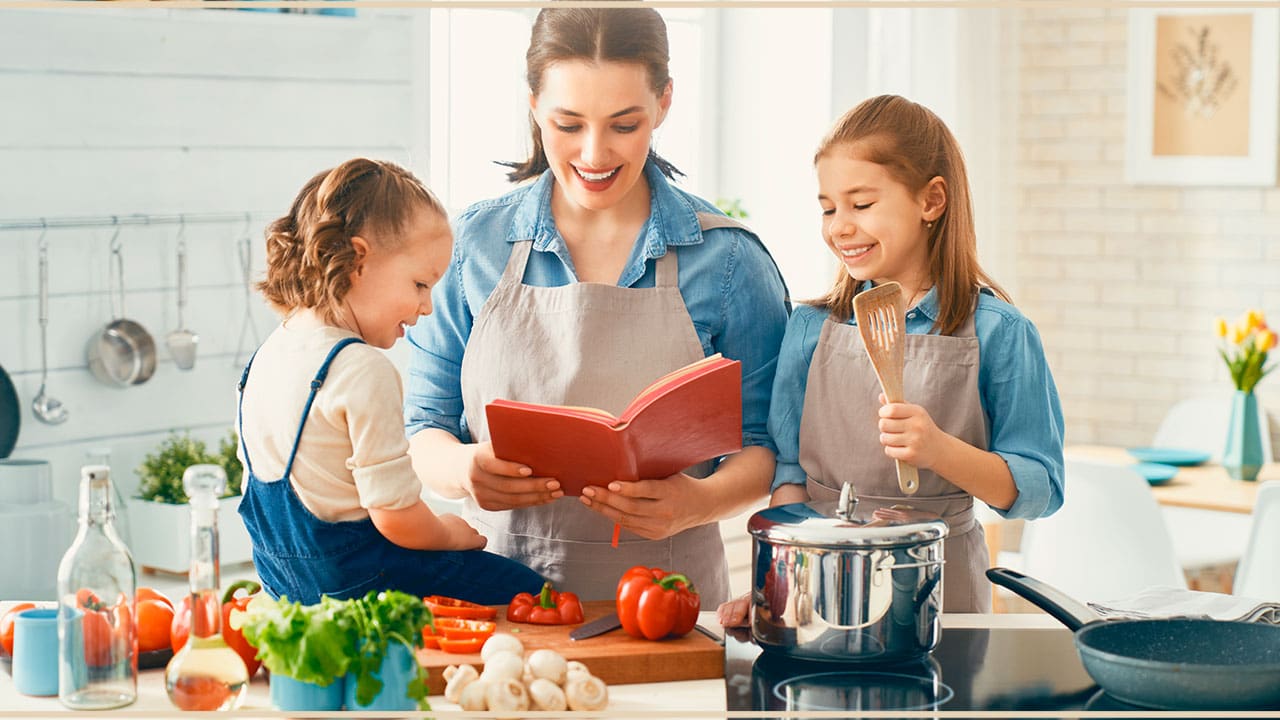 Mãe e filhas cozinhando com caderno de receitas