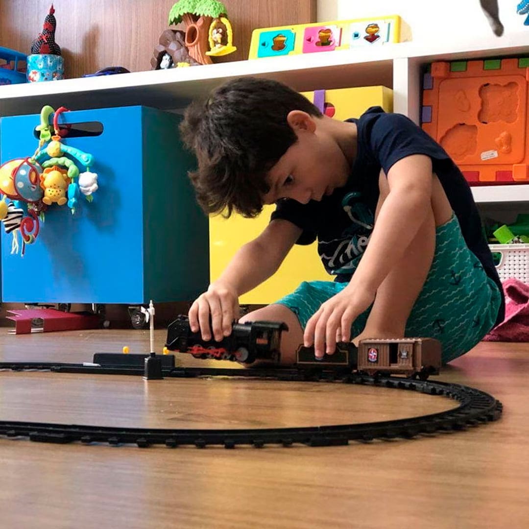 garoto menino criança brincando trenzinho ferrorama mãos piso chão marrom fundo quarto infantil brinquedos