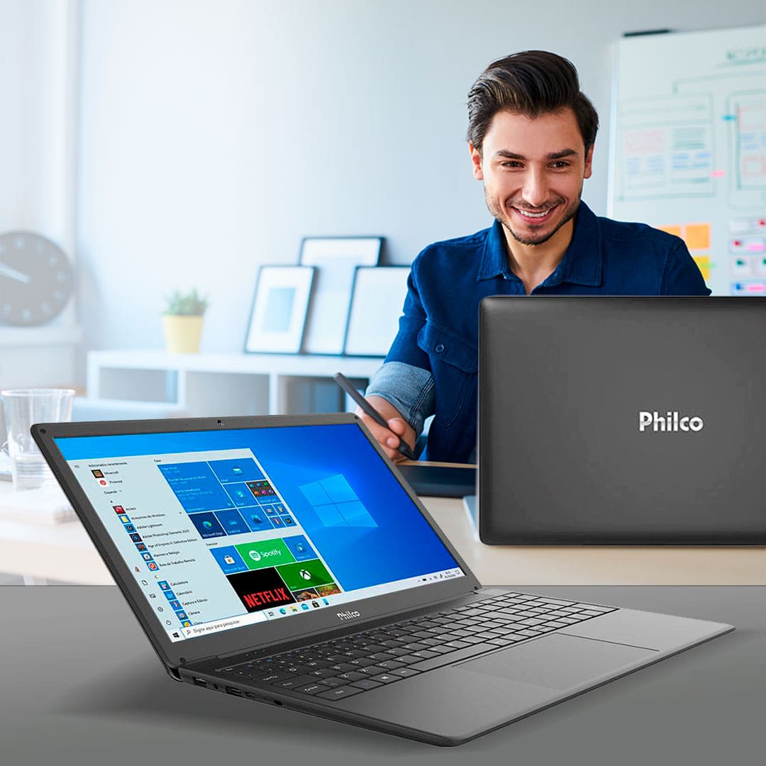 computador philco rapaz homem sorrindo caneta anotação lousa quadros relógio parede flores vaso planta copo xícara