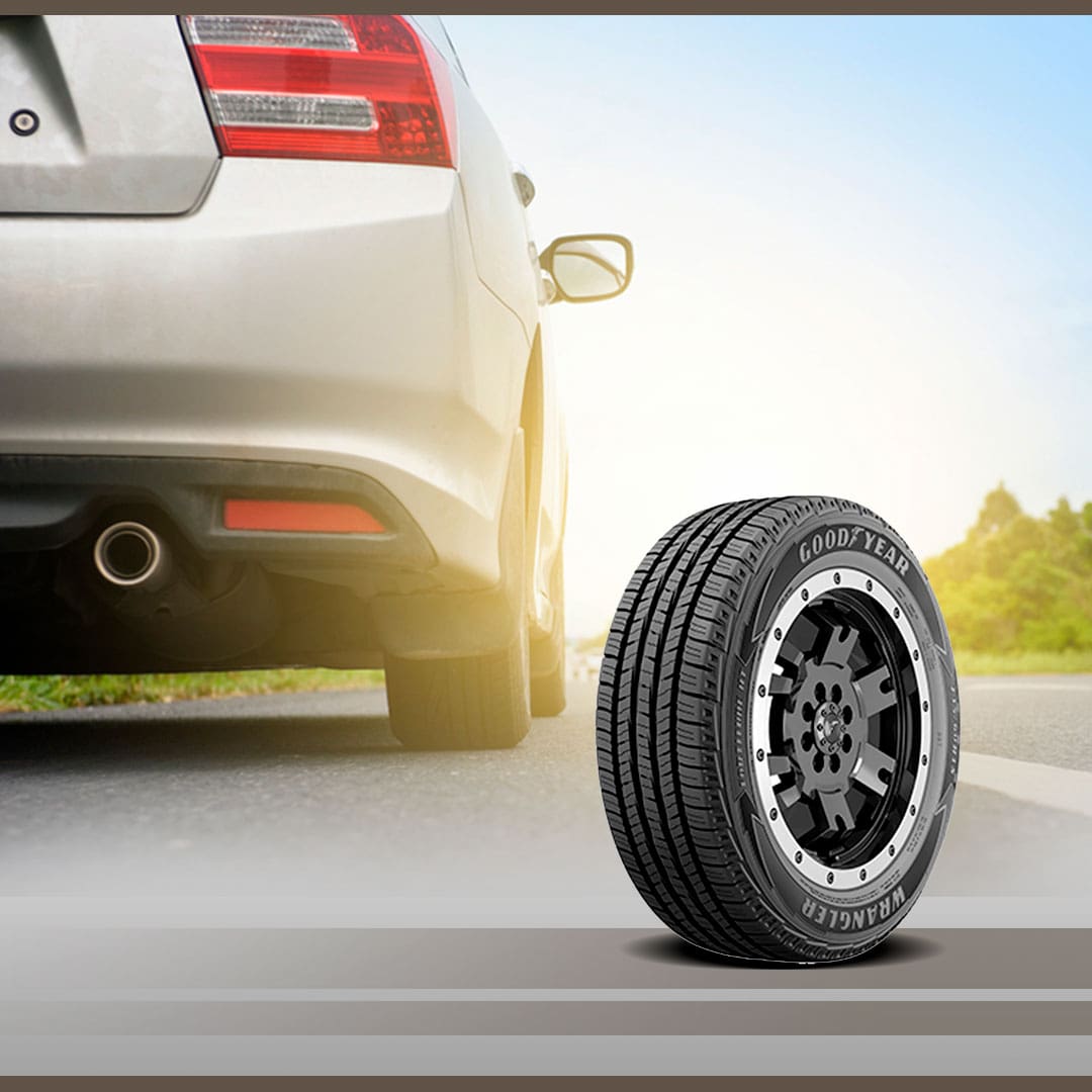 Imagem frente frontal Pneu Goodyear Wrangler Fortitude preto em pé rodovia estrada asfalto cinza mato árvores lateral céu azul carro passeio veículo retrovisor escapamento 