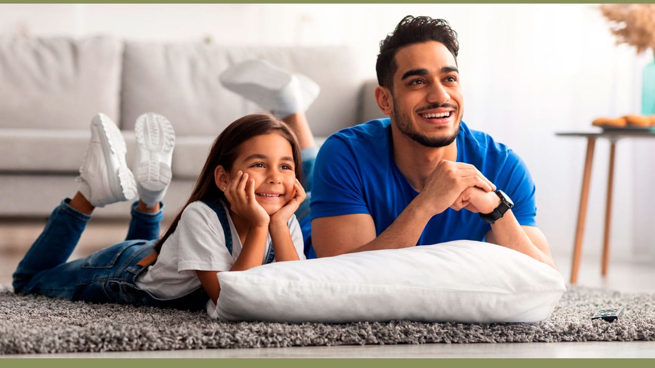 Pai e filha deitados no tapete assistindo TV