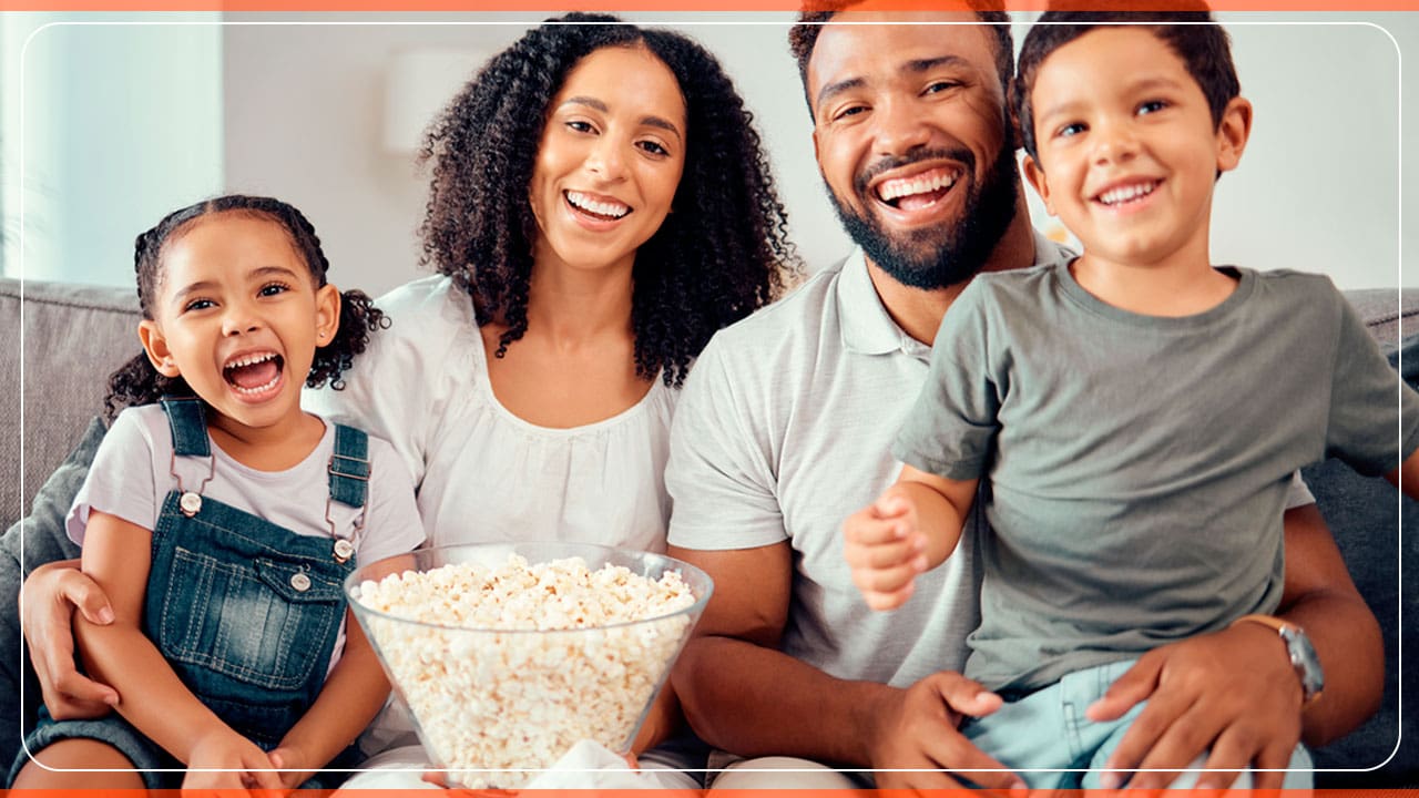 família negros mulher homem jovem menino menina crianças sorrindo pipoca vasilhame pote transparente colo sofá sala