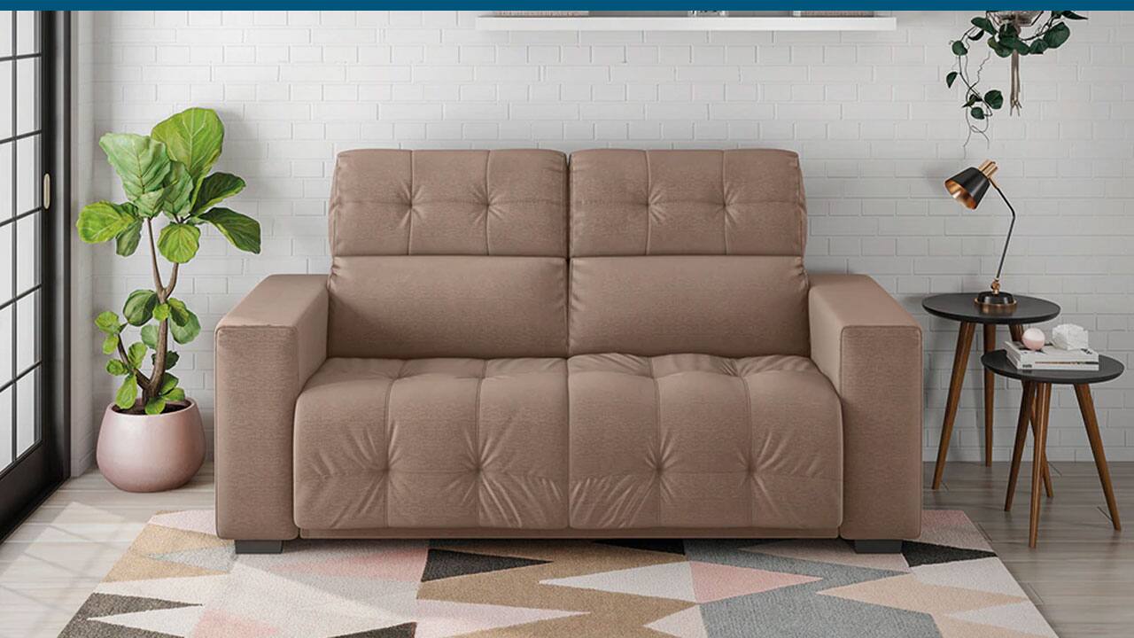 Sofá Hellen Genebra marrom capuccino sala de estar porta lateral tapete colorido vaso planta verde parede branca tijolos prateleiras objetos decorativos luminária pequena mesas pequenas mesinhas