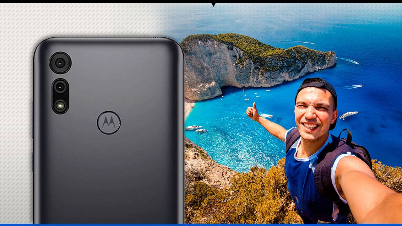 Rapaz fazendo selfie na praia, com o Moto E6i ao lado